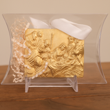 Gold relief sculpture of a religious scene in a clear display case on a wooden surface.