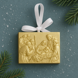 Gold nativity scene ornament with white ribbon on a green background